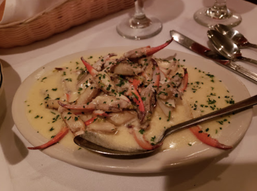 A plate of crab meat in a creamy sauce, garnished with red pepper strips and parsley, served on a white tablecloth.