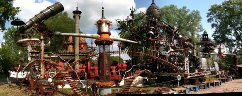 A large, intricate steampunk-inspired sculpture garden with metal structures, gears, and whimsical designs under a blue sky.