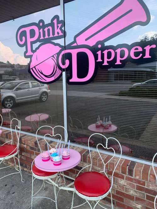 A storefront with a sign reading "Pink Dipper" and colorful ice cream cups on a table outside.