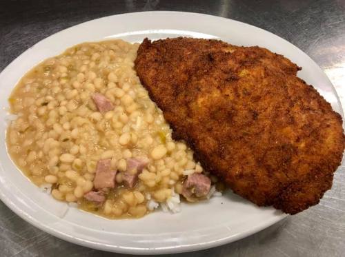 A plate featuring a large fried fish fillet alongside a serving of white beans and rice.