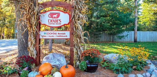 Sign for Dixies Coffee House with pumpkins, flowers, and corn stalks in a scenic outdoor setting.