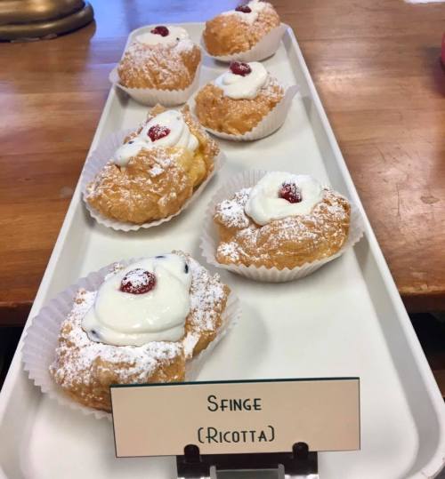 A tray of Sfinge pastries, topped with cream and a cherry, dusted with powdered sugar.