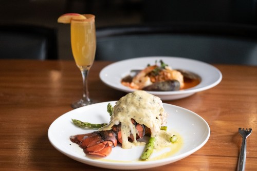 A plate of lobster with asparagus and creamy sauce, with a mimosa and another dish in the background.