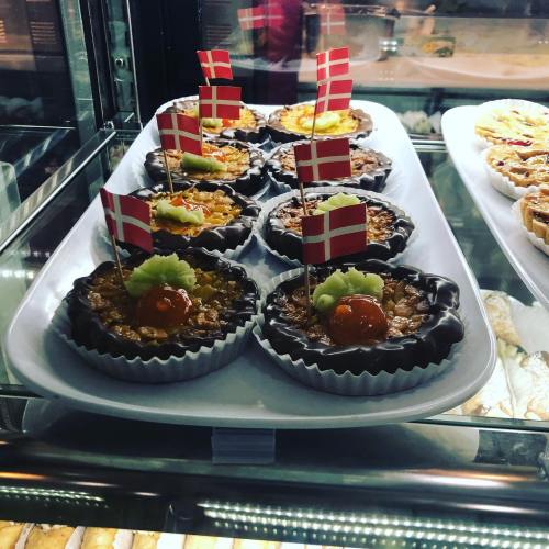 A display of chocolate tarts topped with green garnish and small Danish flags in a pastry case.