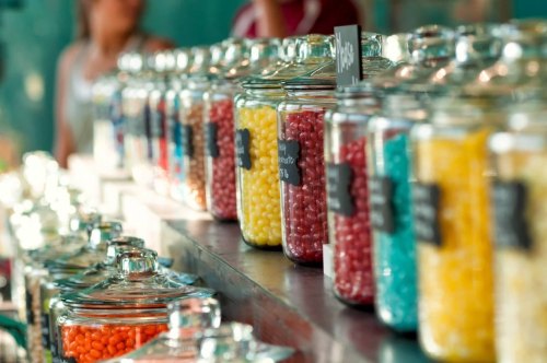 Colorful jars filled with various candies line a counter, with labels indicating different flavors.