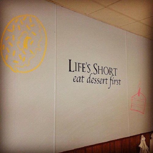 A wall with the quote "Life's Short eat dessert first" and colorful drawings of a donut and a cake.