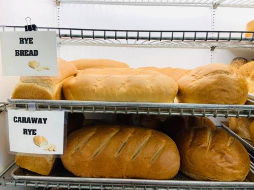 Loaves of rye bread and caraway rye displayed on metal shelves in a bakery.