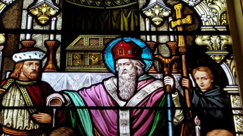 Stained glass depicting a bearded figure in a red and blue robe, flanked by two others in historical attire.