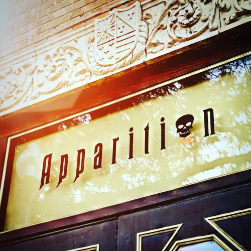 Sign reading "Apparition" with a skull graphic, set against an ornate building facade.