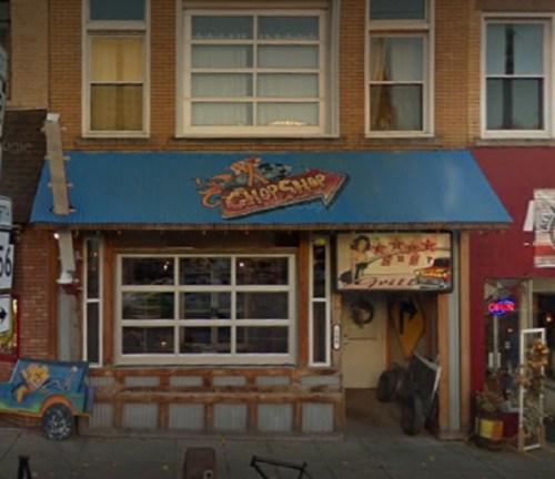 A colorful storefront with a blue awning, featuring signs for a barbershop and a vintage car mural.