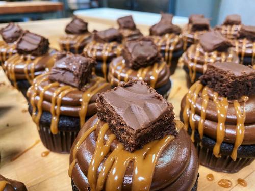 Close-up of chocolate cupcakes topped with chocolate frosting, caramel drizzle, and a brownie piece.
