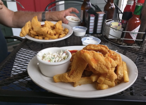 A plate of fried fish and fries with coleslaw, alongside a bowl of dipping sauce and a plate of fried snacks.