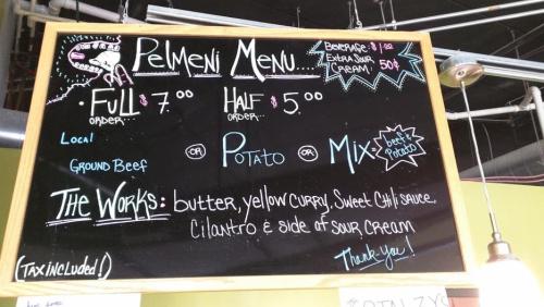 Chalkboard menu for pelmeni: full order $7, half order $5, options include ground beef, potato, or mix with toppings.