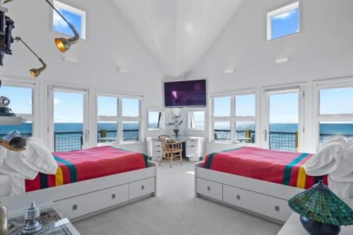 Bright coastal bedroom with two beds, large windows, and a view of the ocean. Modern decor and natural light enhance the space.