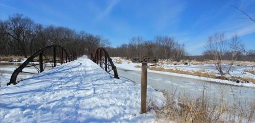 A snowy landscape featuring an old bridge labeled "Bridge 4" with a frozen river and bare trees in the background.