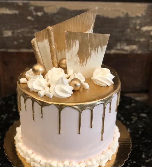 A beautifully decorated cake with a gold drip, topped with white frosting, gold spheres, and elegant gold accents.