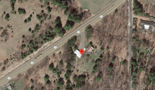 Aerial view of a rural area with a building labeled "Gourmet Garage" near a road and surrounded by trees.
