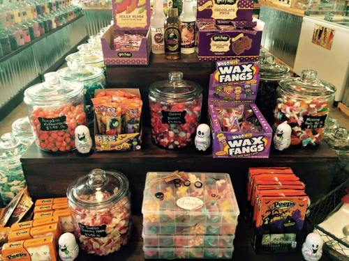 A colorful display of various candies in jars and boxes, including gummies, wax fangs, and Peeps, in a shop setting.