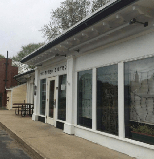 Exterior of The Metro Bistro, featuring large windows and a white facade, with a picnic table nearby.