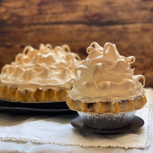 Two pies with fluffy meringue topping on a rustic wooden background, one slightly in front of the other.