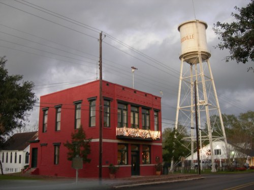 A red brick building with a sign, next to a tall white water tower, under a cloudy sky.
