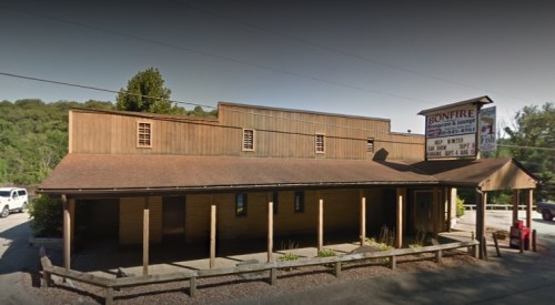 A wooden building with a sign for "Bonfire" and a porch, surrounded by trees and parked cars.