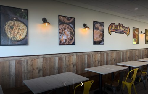 Interior of a restaurant with wooden walls, tables, and framed photos of macaroni dishes on the wall.