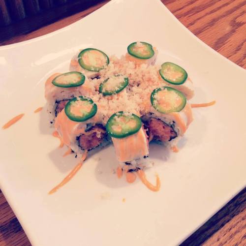A plate of sushi rolls topped with jalapeño slices and drizzled with sauce, served on a white dish.