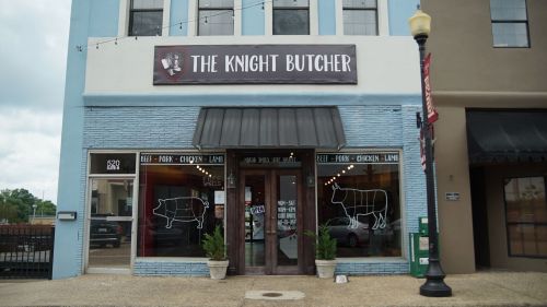 Exterior of "The Knight Butcher" shop, featuring a sign and window displays of various meats.
