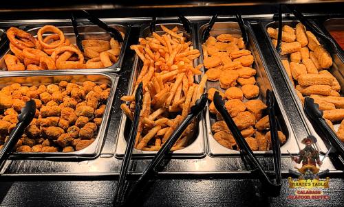A buffet display featuring fried foods: onion rings, French fries, and chicken nuggets in metal trays.