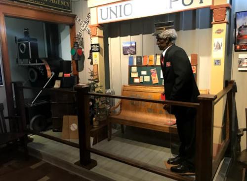 A museum display featuring a vintage train station with a mannequin in a suit and historical artifacts.