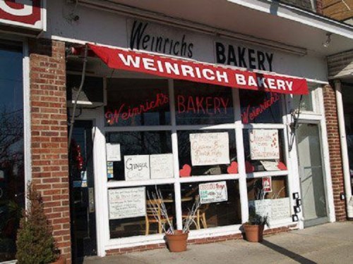 Exterior of Weinrich Bakery, featuring a red awning and large windows with handwritten signs and decorations.