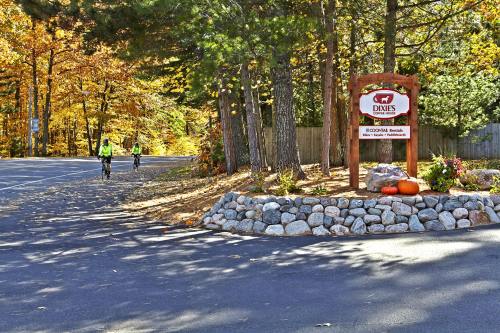 A scenic road with cyclists, colorful autumn trees, and a sign for Dixie's, surrounded by a stone border and pumpkins.