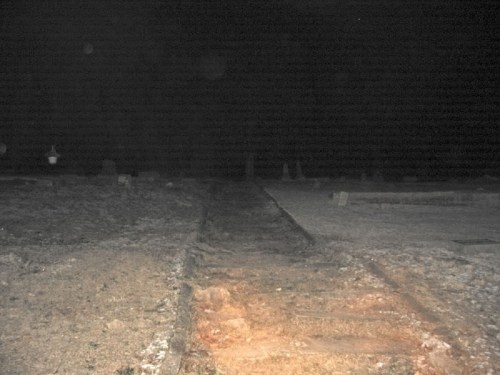 A dimly lit path through a graveyard at night, with gravestones visible in the background.