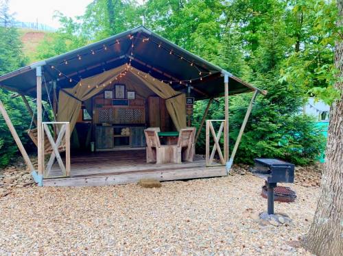 A cozy outdoor cabin with string lights, wooden chairs, and a grill, surrounded by greenery and gravel.