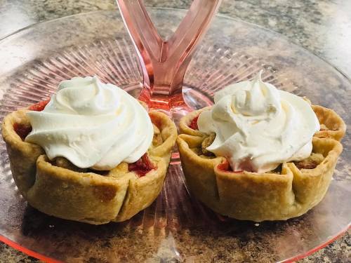 Two mini fruit pies topped with whipped cream, sitting on a pink glass plate.