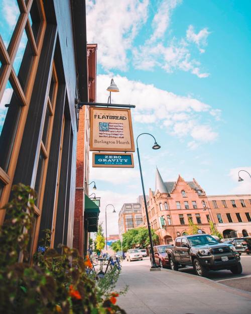 A street view featuring a restaurant sign, flowers, and historic buildings under a blue sky with scattered clouds.