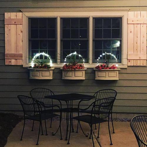 A cozy outdoor seating area with a table and chairs, featuring a window with illuminated flower boxes at night.
