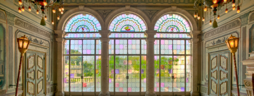 Colorful stained glass windows in an ornate room, with decorative walls and a view of greenery outside.