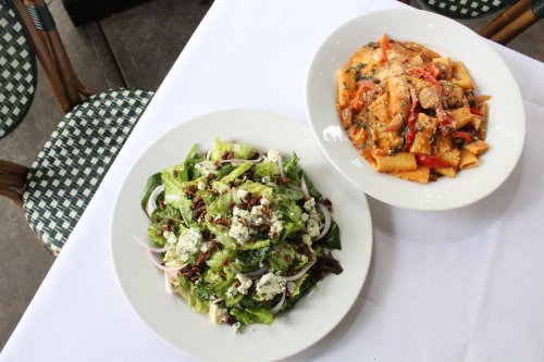 A fresh salad with greens and cheese beside a plate of pasta with vegetables in a creamy sauce.