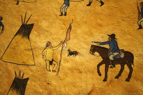 A historical mural depicting a Native American holding a flag, with a mounted figure and teepees in the background.