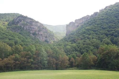 Lush green mountains with steep cliffs and a valley, under a bright sky.