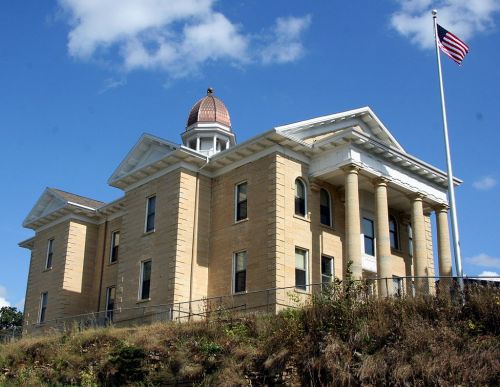 Historic building with a dome and columns, set against a blue sky with an American flag flying nearby.