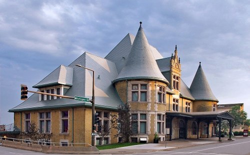 Historic building with pointed roofs and intricate architecture, set against a cloudy sky at a street intersection.