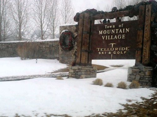 Sign for Mountain Village, Telluride Ski & Golf, surrounded by snow and trees in a winter landscape.