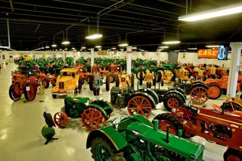 A spacious museum filled with vintage tractors in various colors, showcasing agricultural history and machinery.