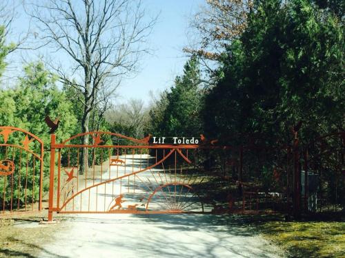 A decorative iron gate with "Lit Toledo" sign, leading to a tree-lined gravel driveway.