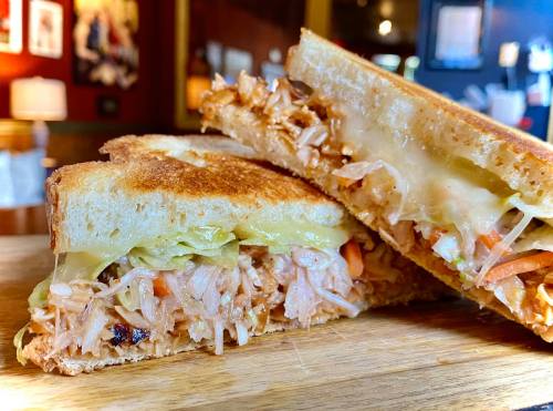 A close-up of a toasted sandwich filled with shredded chicken, vegetables, and melted cheese, served on a wooden board.