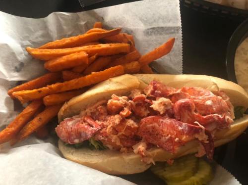 A lobster roll filled with lobster meat on a bun, served with a side of sweet potato fries.