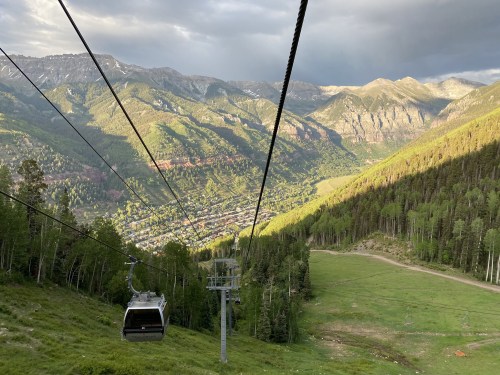 A scenic view from a gondola overlooking a valley surrounded by mountains and lush greenery.
